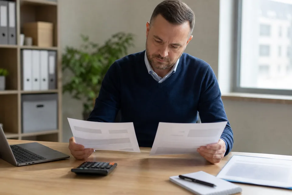 Właściciel firmy porównuje dwie oferty cenowe przy biurku z kalkulatorem