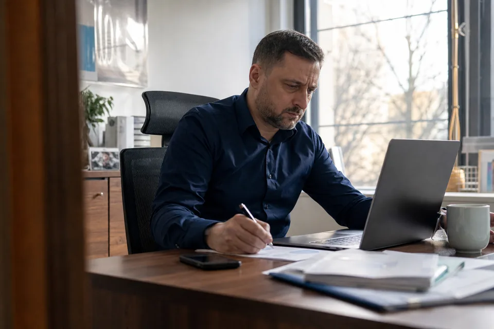 Właściciel firmy przy laptopie przygotowuje zgłoszenie spornego wpisu i robi notatki